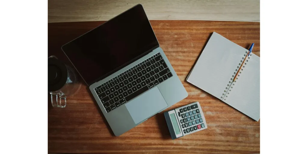 Abrir cuenta bancaria en Suiza como español – ordenador portátil, libreta y calculadora sobre una mesa de madera